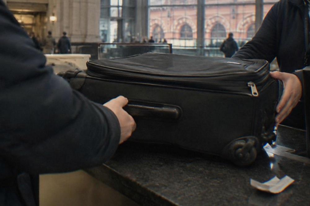 Traveller handing a suitcase across a staffed luggage storage counter in a train station