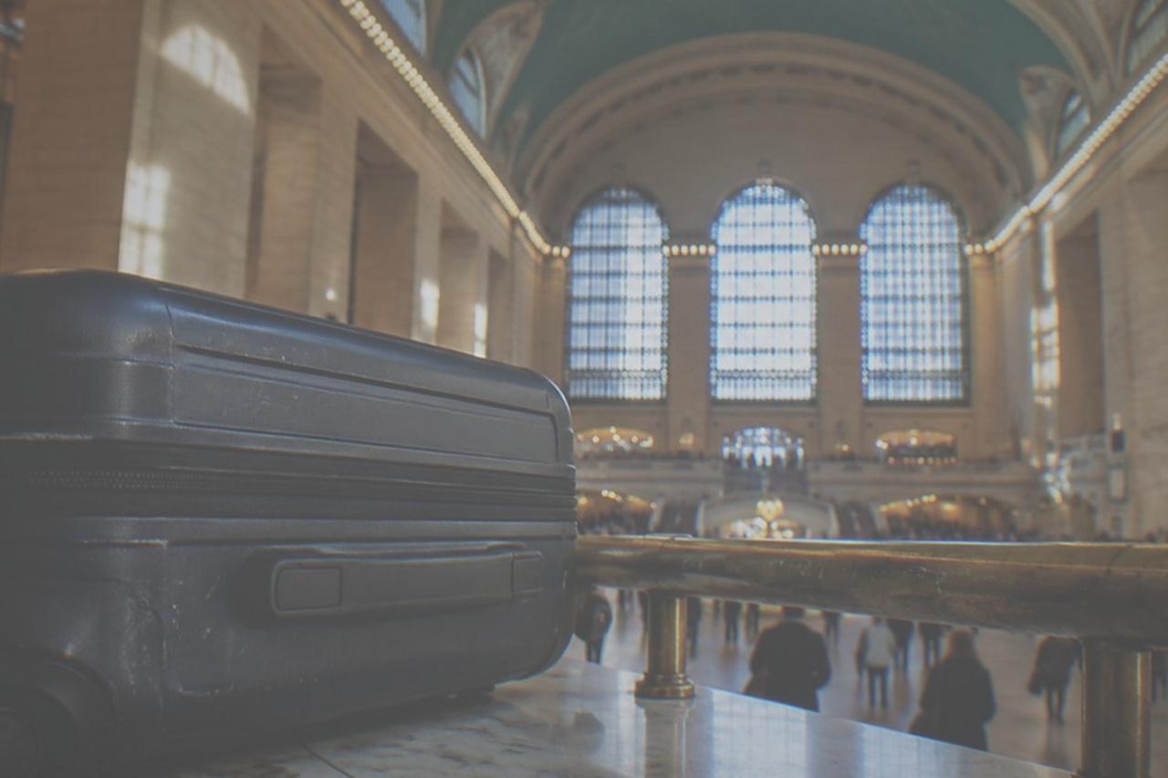 Main concourse of Grand Central Terminal with sunlight through arched windows and a clock above an information booth