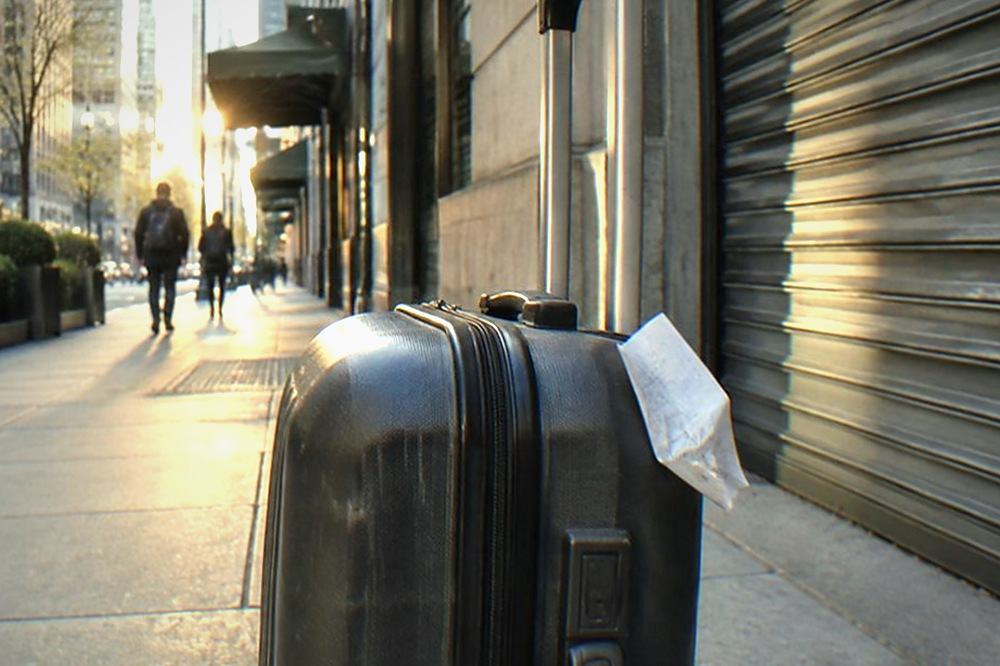 An empty midtown Manhattan sidewalk with a suitcase standing beside a closed shopfront