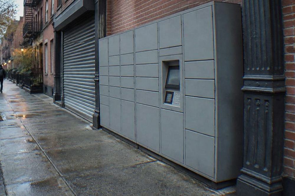 Row of grey metal parcel lockers built into a city sidewalk next to a closed shopfront