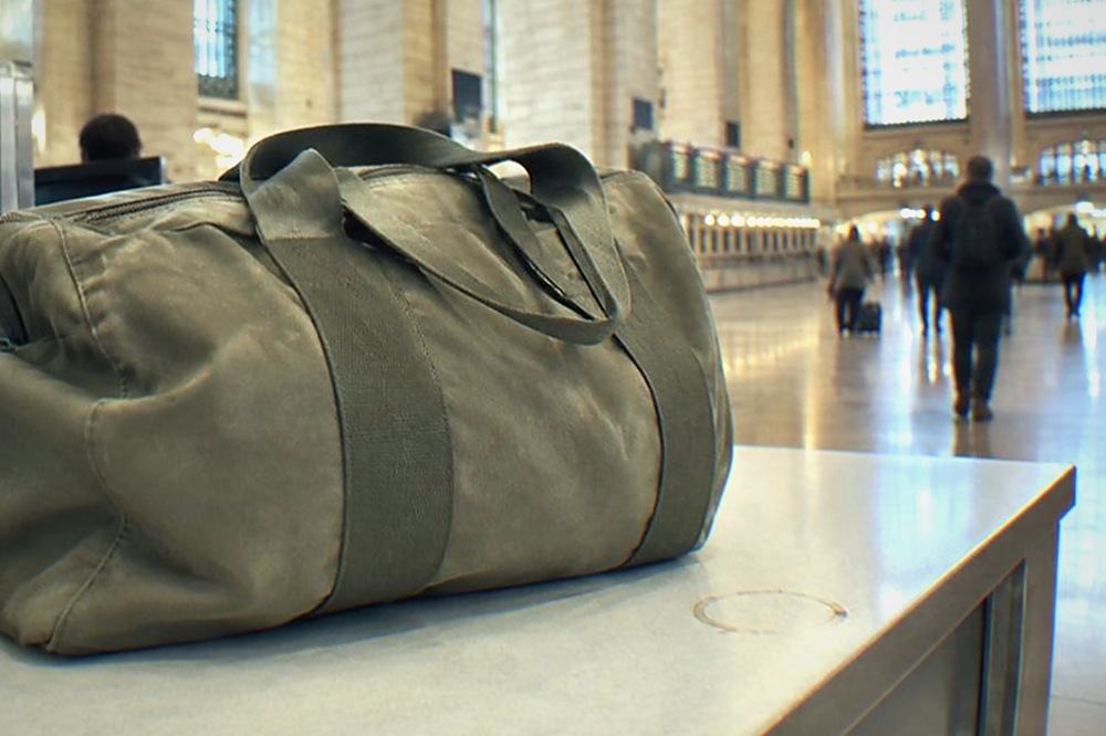 A customer service desk in a bright train hall with a traveller standing beside a suitcase asking a question