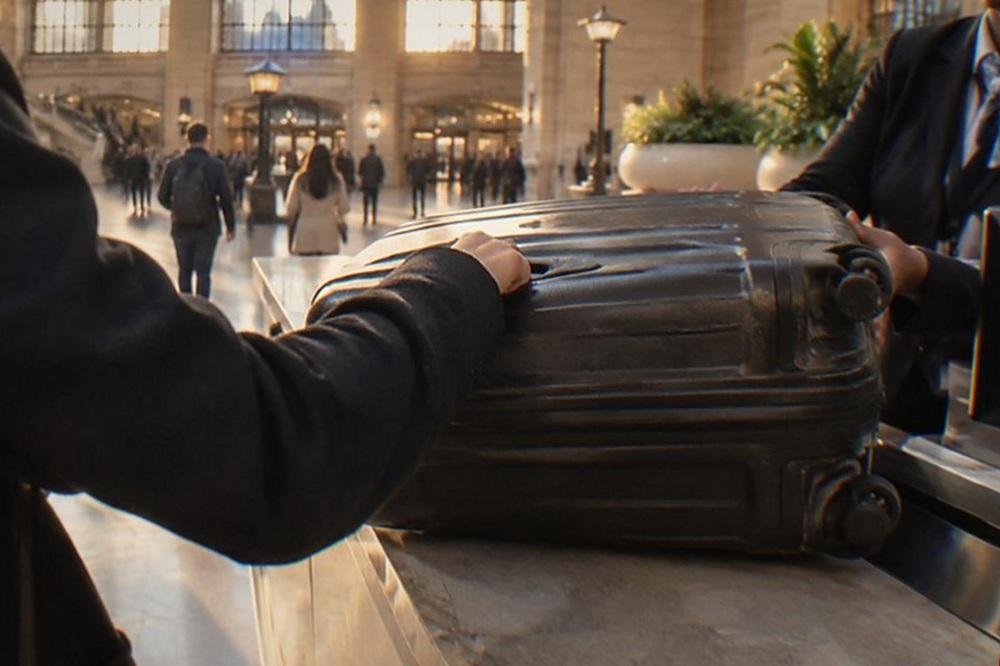 Traveller handing a suitcase across a staffed service counter in a bright train hall