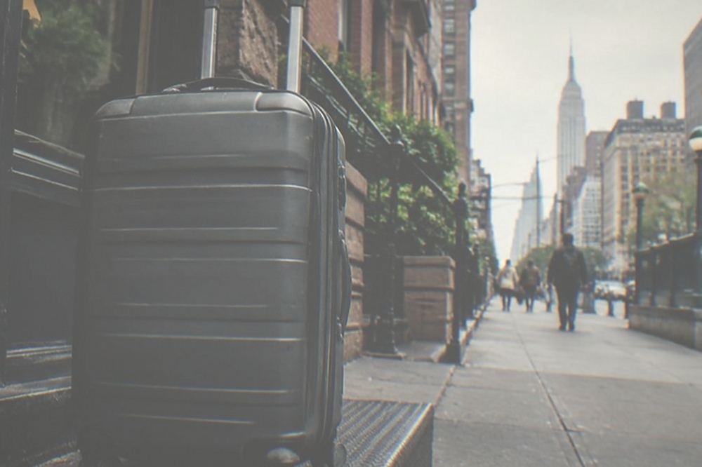 Rolling suitcase parked beside a shop counter on a Manhattan sidewalk near Penn Station