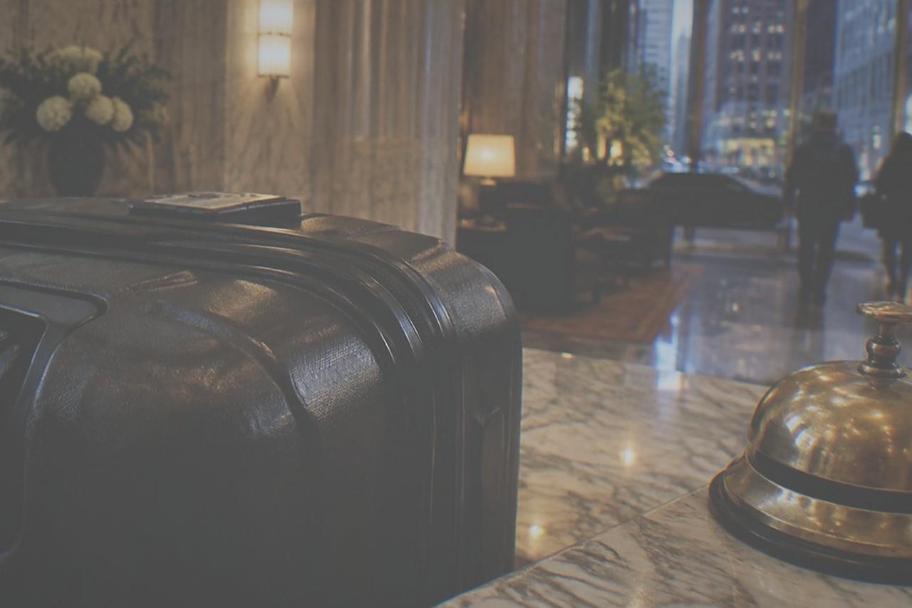 Hotel front desk with a bell and a suitcase parked beside the counter in a marble lobby