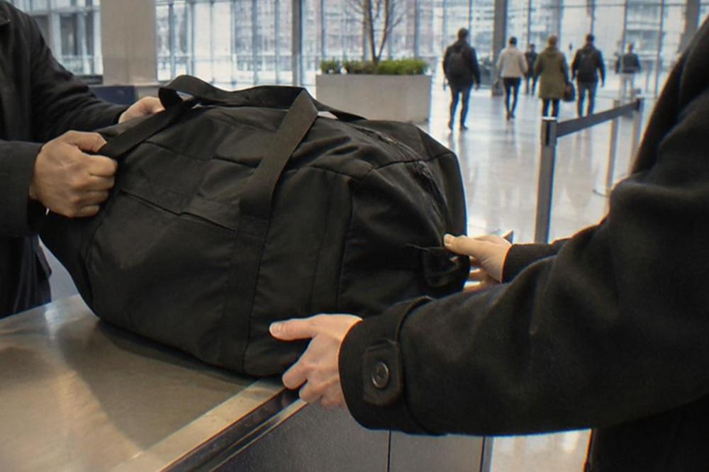 A service counter in an airport terminal with a staff member assisting a traveller with a suitcase