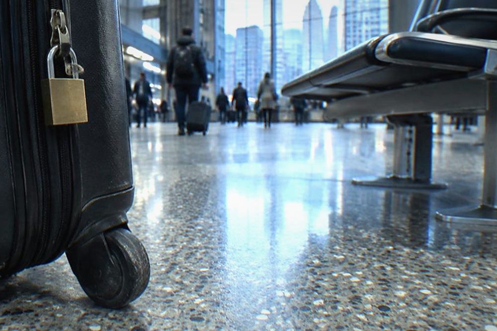 A locked suitcase and a padlock resting on an airport terminal floor beside seating