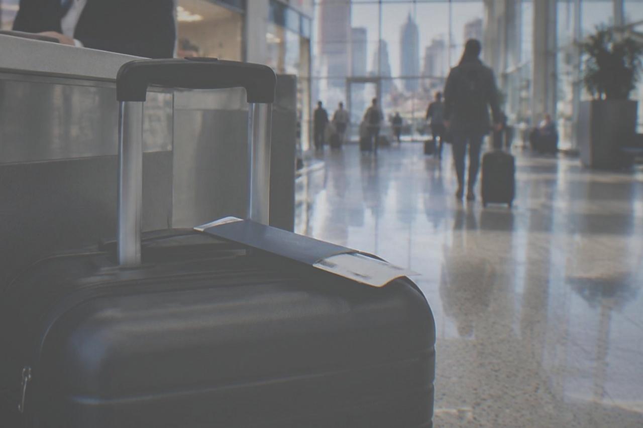 An airport terminal concourse with a service counter and travellers rolling suitcases past shopfronts