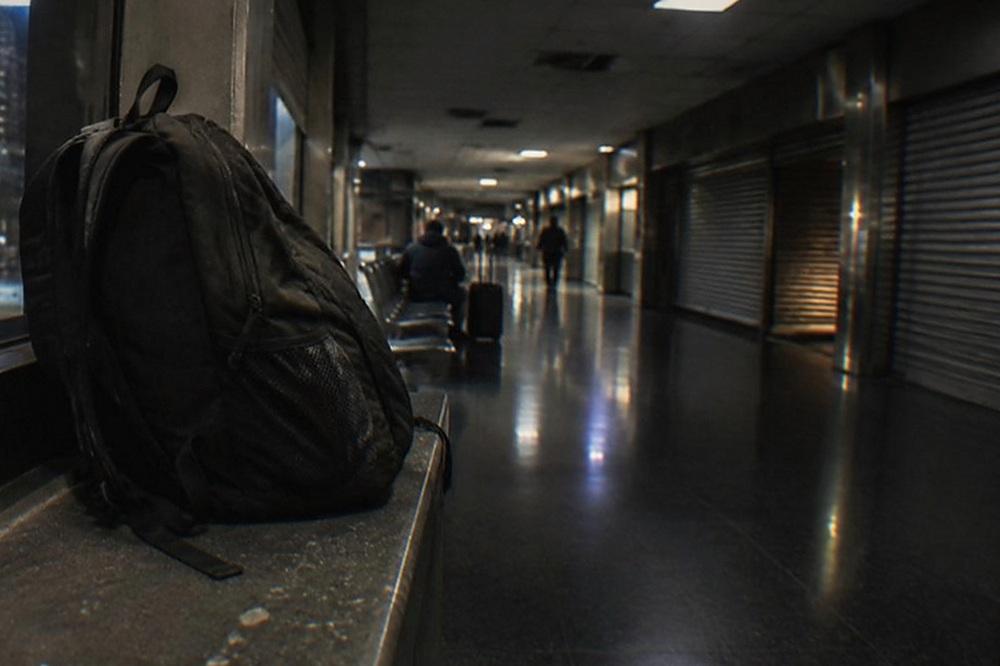 Dimly lit airport terminal corridor with a lone traveller seated near closed shopfronts.