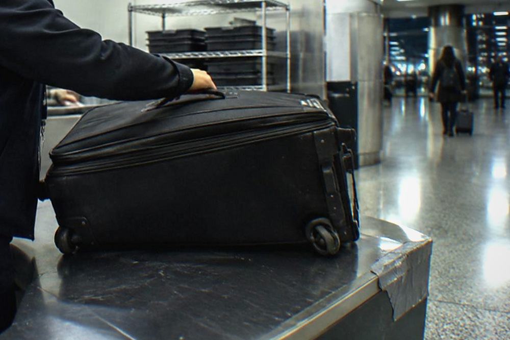 Airport baggage storage counter with a staff member assisting a traveller with a suitcase.