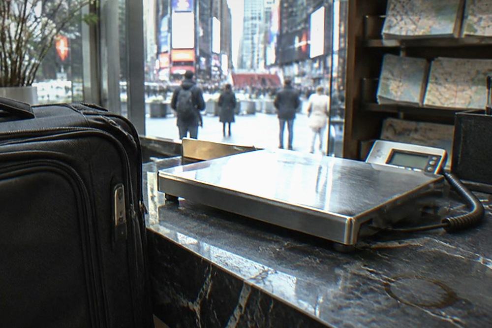 Empty hotel lobby desk with a luggage scale and shelves of folded maps in the background