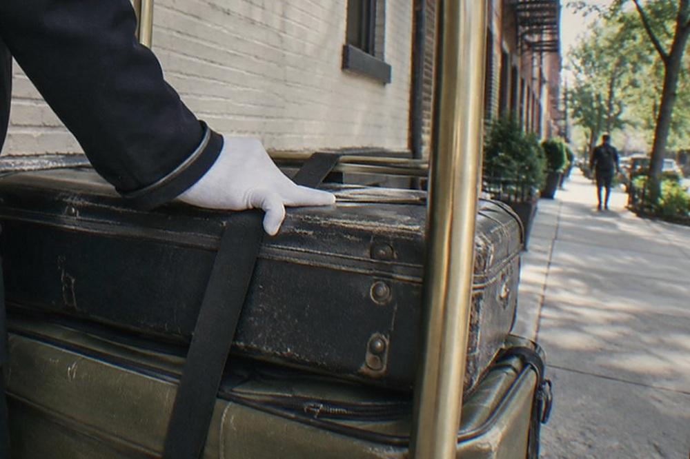 Bellhop uniform with white gloves beside a stacked luggage cart in a hotel corridor