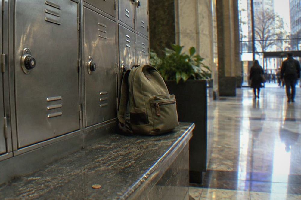 A row of metal day lockers with coins and a small backpack on a bench