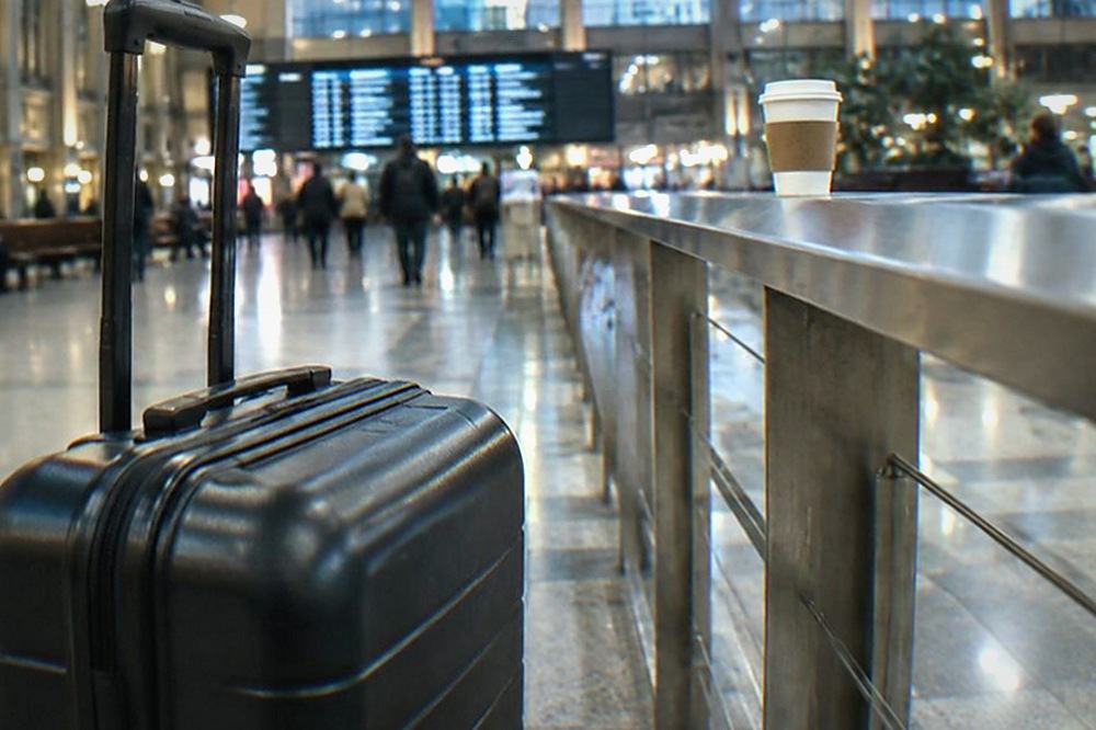 Long rail concourse with departures board, benches and travellers pulling rolling suitcases