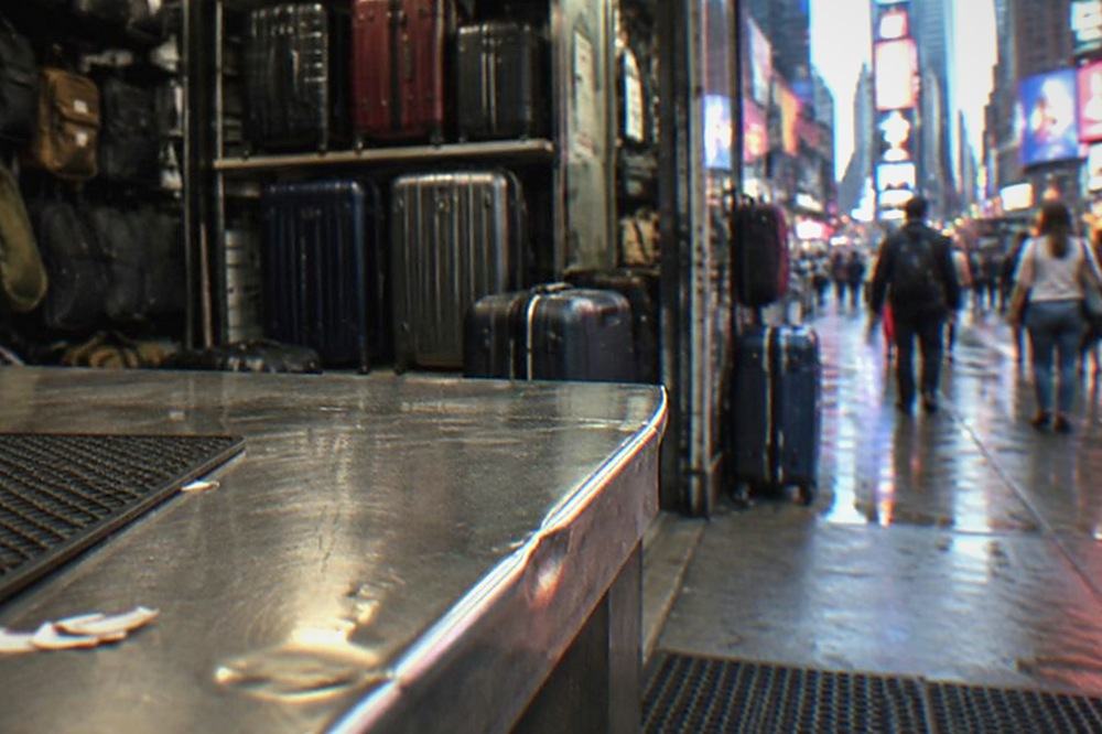 A shop counter in a busy Manhattan station area with bags behind it
