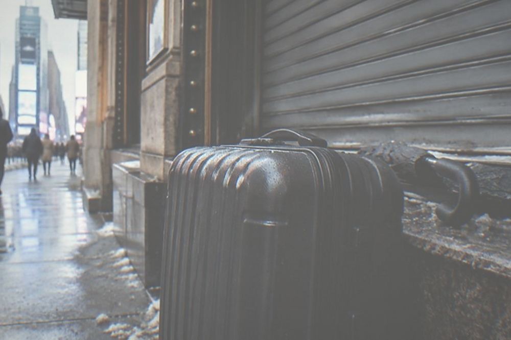 Wide sidewalk beside a theater with a rolling suitcase parked against a wall next to a closed door