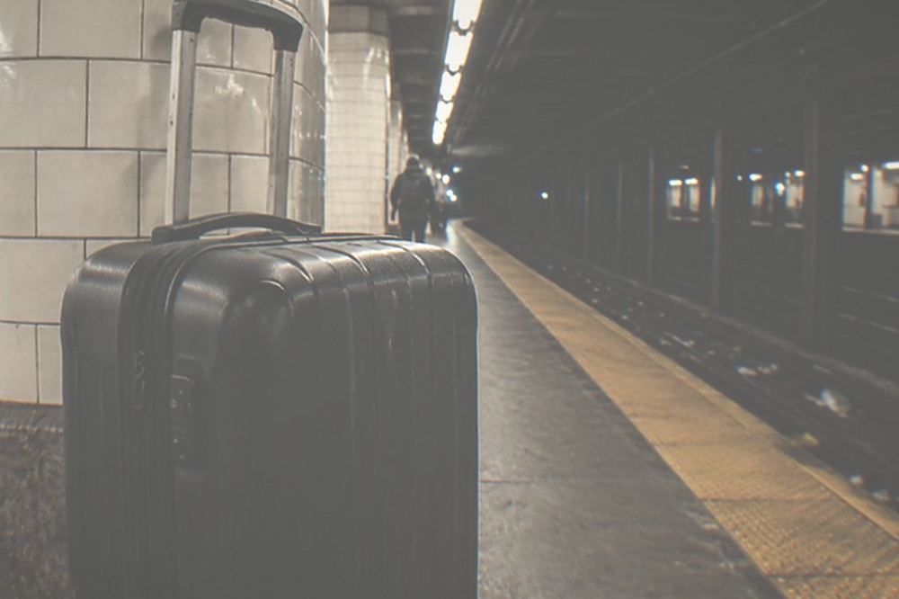 Empty subway platform late at night with a standing suitcase beside a tiled column and no people visible