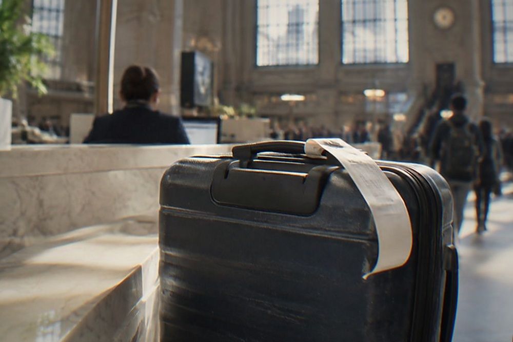 A staffed customer service desk in a bright train hall with a suitcase parked beside the counter