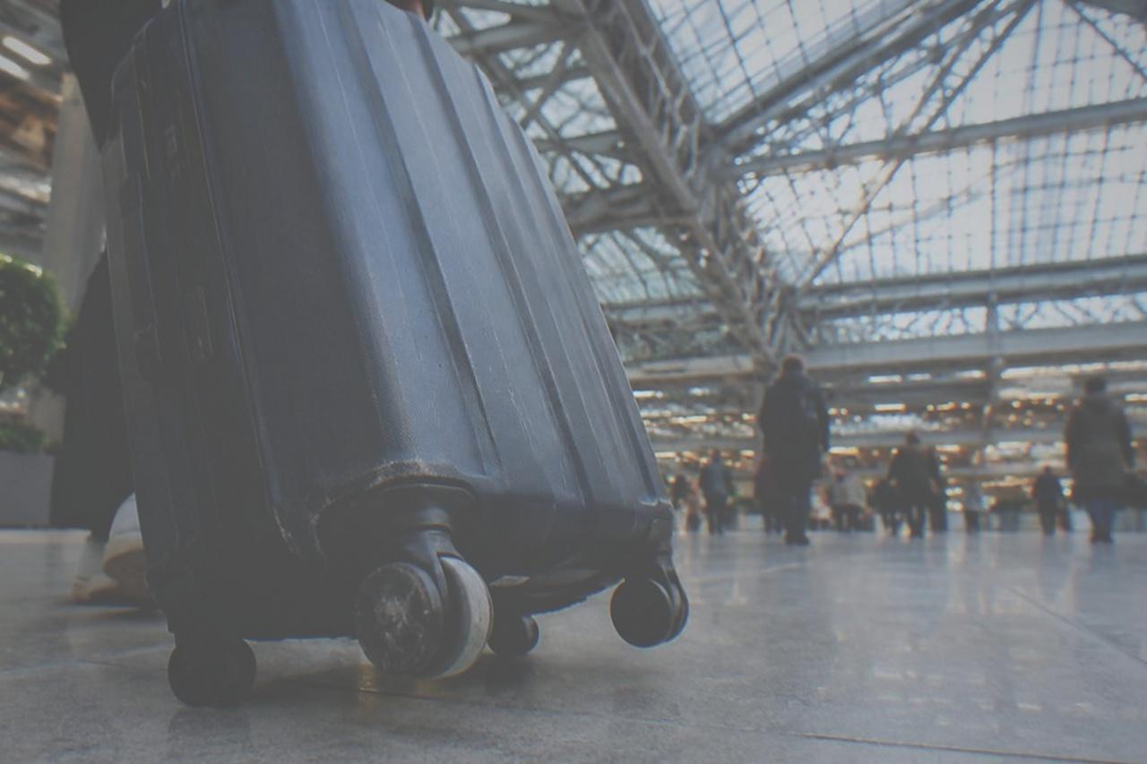 The high glass atrium of a train hall with a traveller rolling a suitcase across the concourse floor