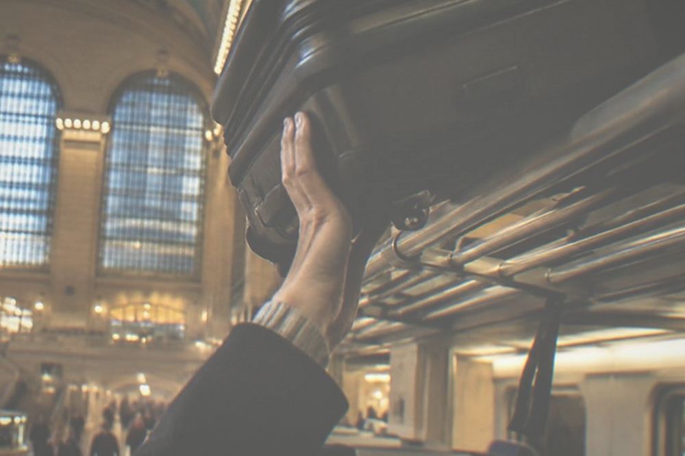 A heavy suitcase being lifted onto an overhead luggage rack on a train