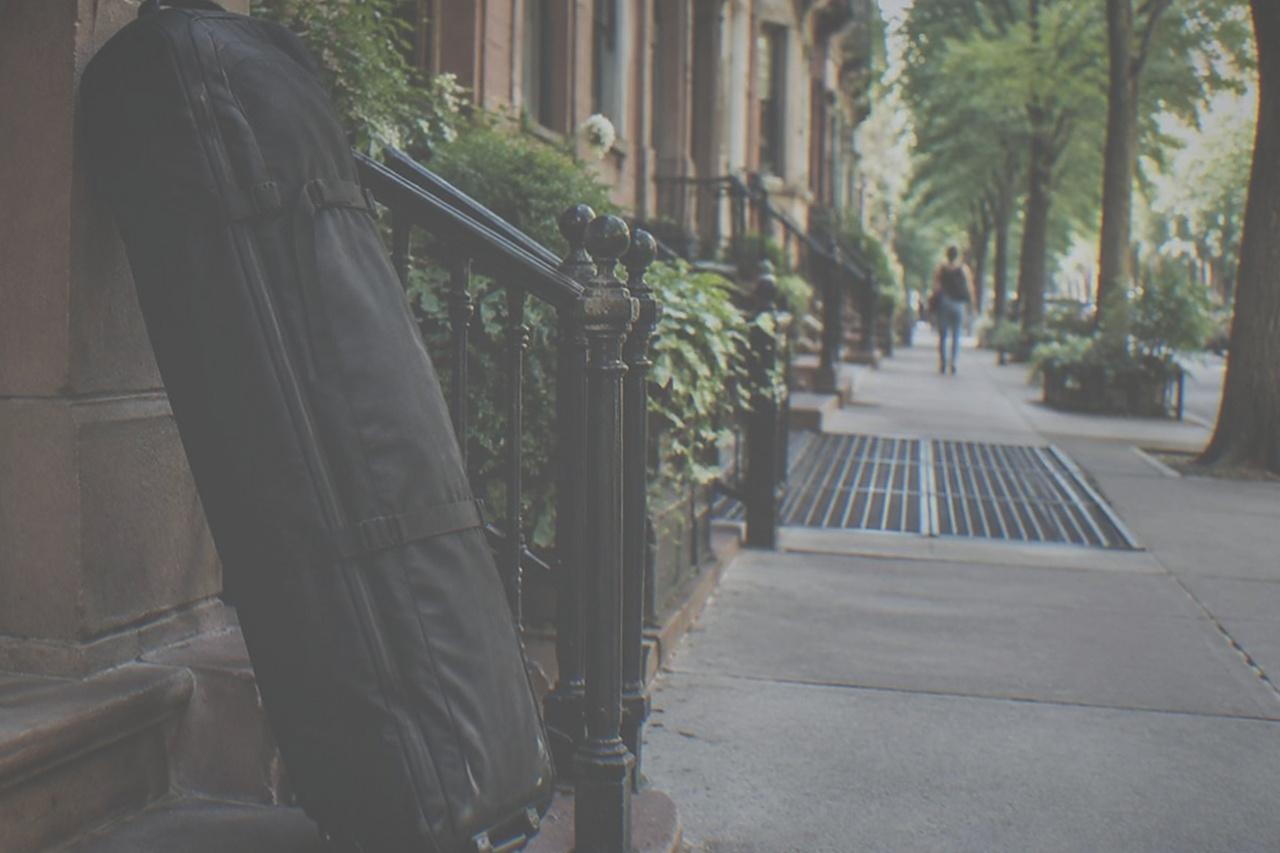 A large wheeled suitcase standing beside a doorway on a quiet New York side street