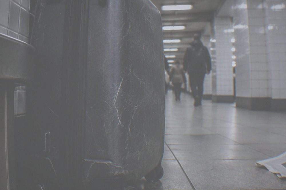 Traveller pulling a wheeled suitcase through a tiled subway station corridor