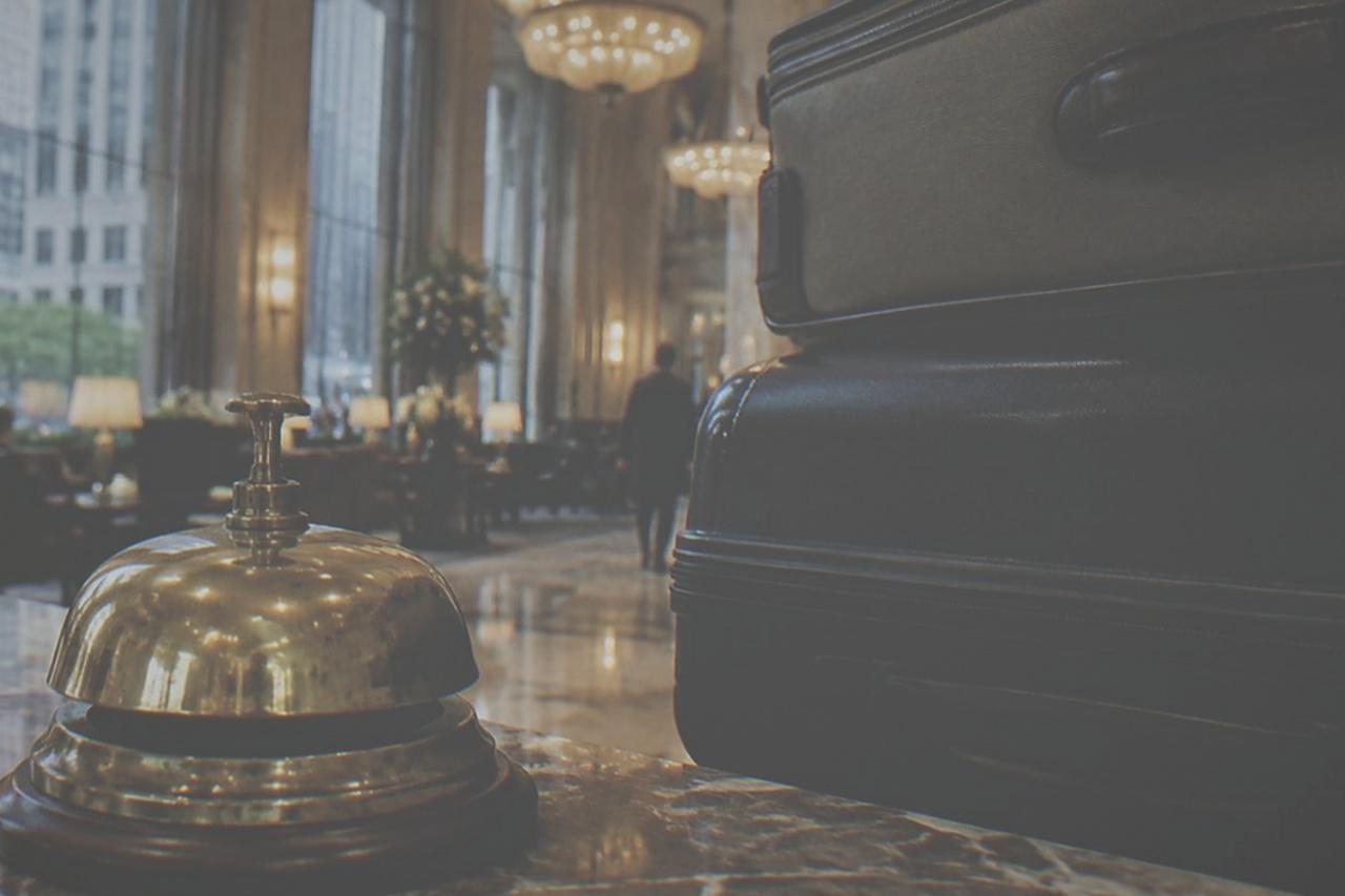 Empty hotel bell desk counter with brass bell and stacked suitcases in a marble lobby
