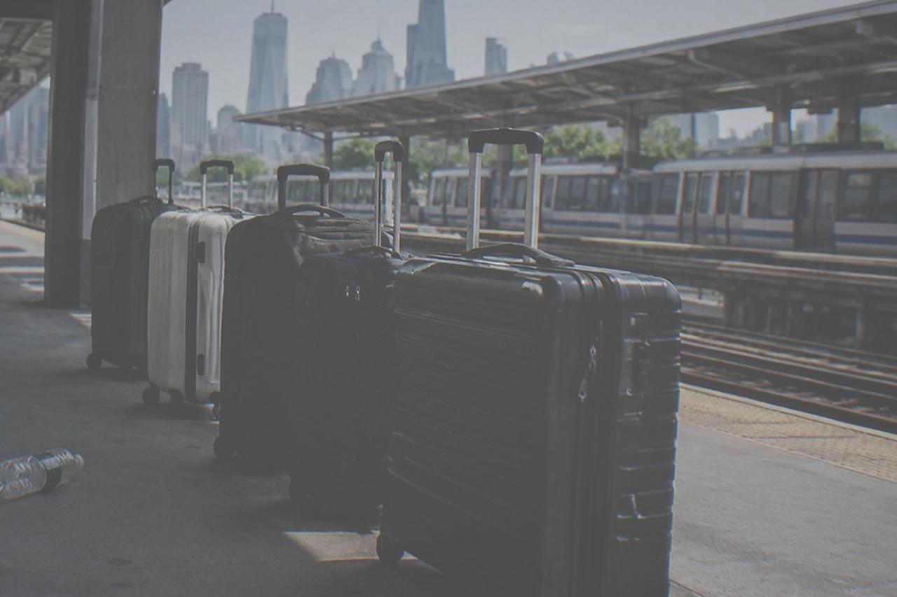 An AirTrain station platform at a New York airport with a row of seated suitcases waiting beside the track