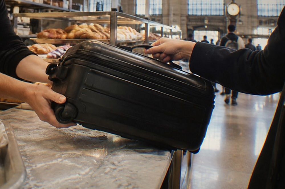 A staffed shop counter in New York with a suitcase being handed over and a numbered tag clipped to the handle.