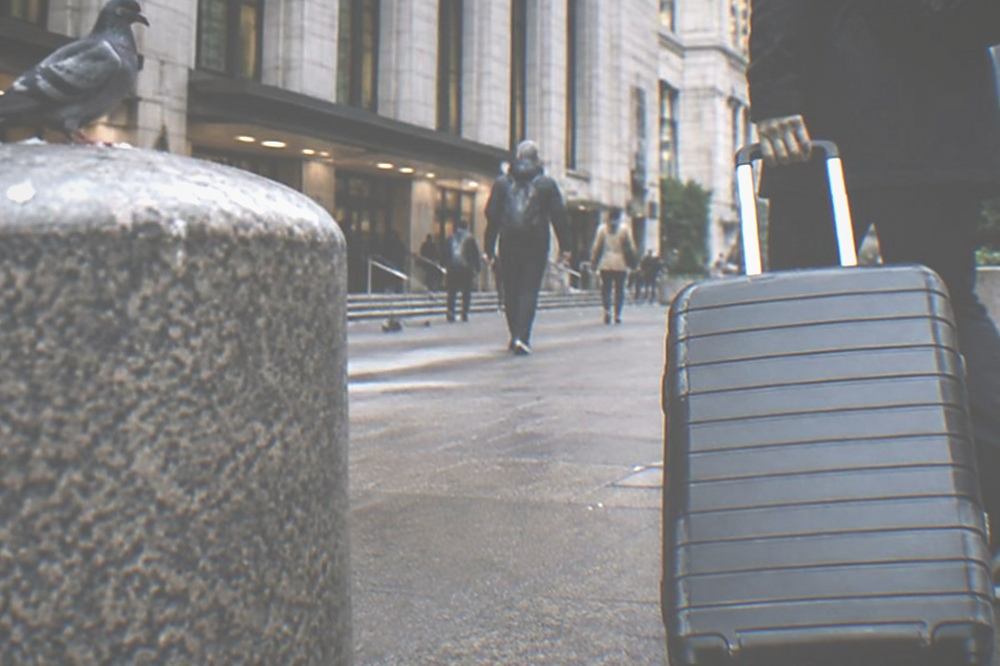 A traveller pulling a suitcase across the street from a large train station entrance in Manhattan
