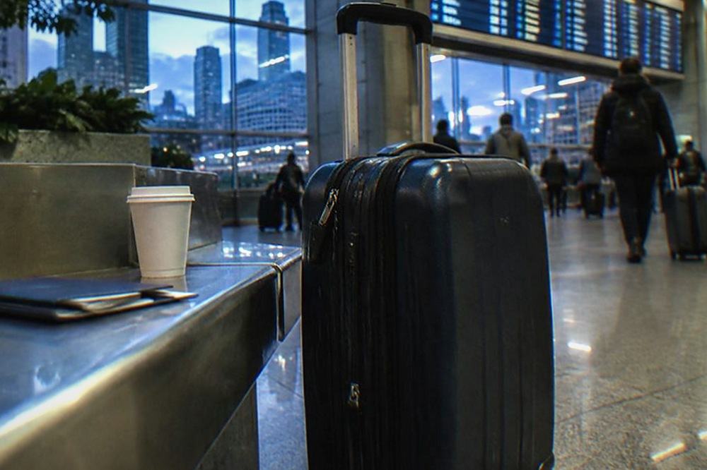 Traveller standing in an airport terminal with a suitcase beside a departure board