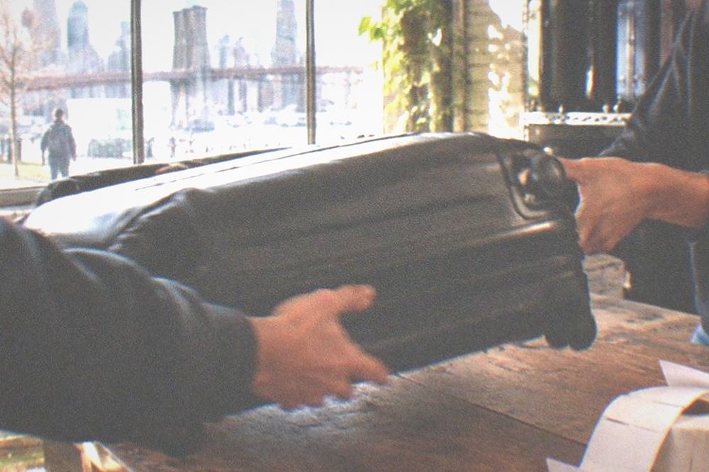 Traveler handing a suitcase across a shop counter to a staff member