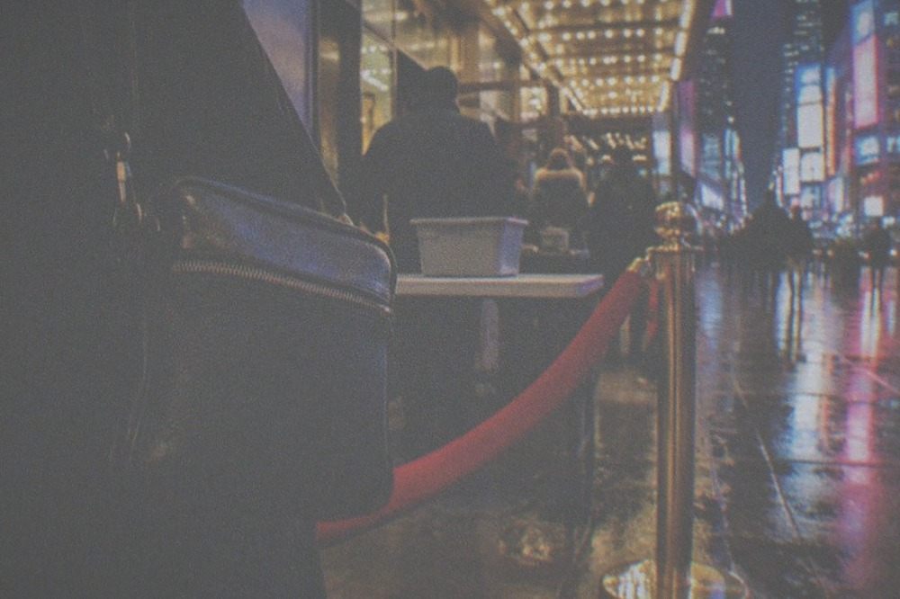 Theatre entrance at night with visitors carrying small bags through security