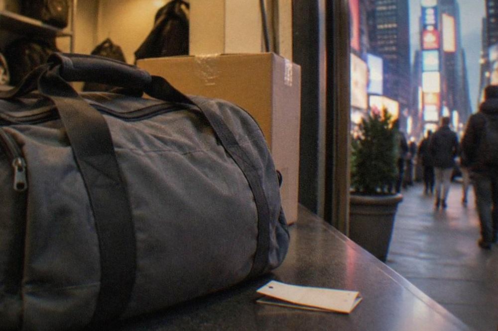 A staffed bag storage counter inside a small Manhattan shop, a folded claim ticket and a suitcase on the counter, warm interior light