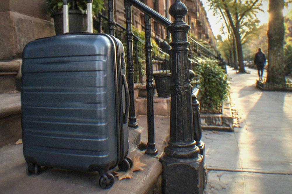 A row of brownstone front steps in Brooklyn with a suitcase waiting at the bottom step, late afternoon light between buildings