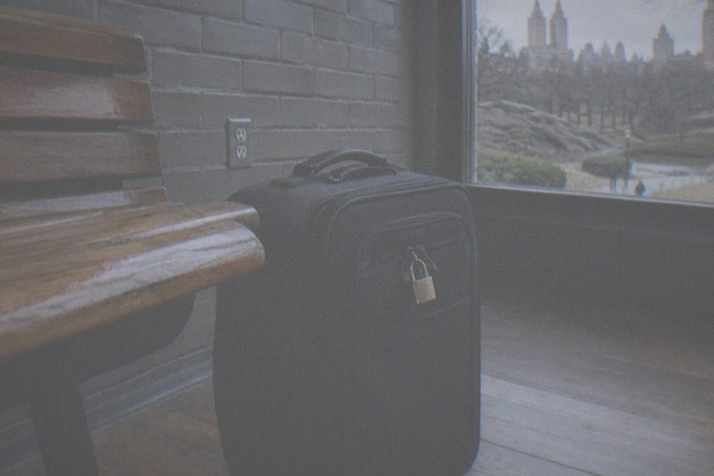 A padlocked soft-sided suitcase standing closed on a wooden floor beside a wall outlet with no cable plugged in