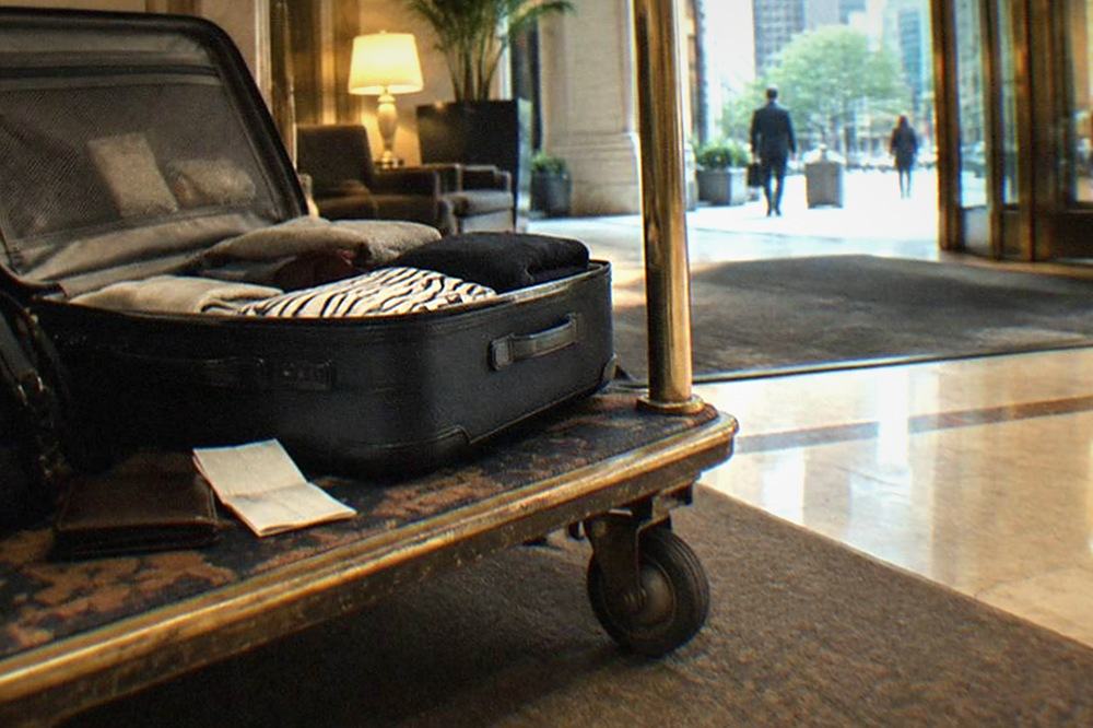 Open suitcase on a hotel luggage cart beside a receipt and a wallet on a wooden floor