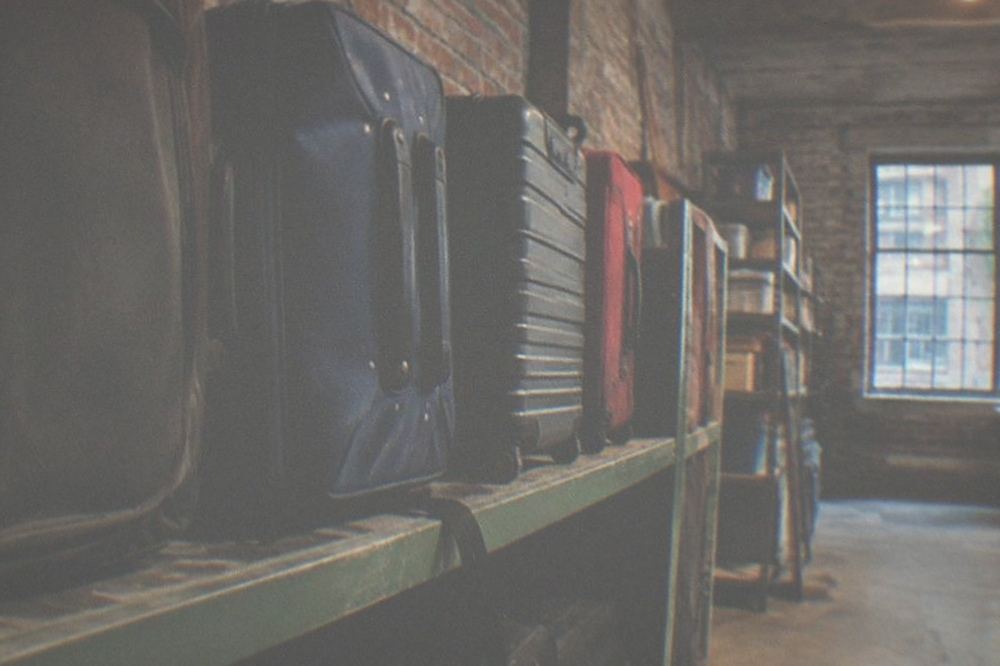 Suitcases lined up against a wall in a storage room with shelves behind them