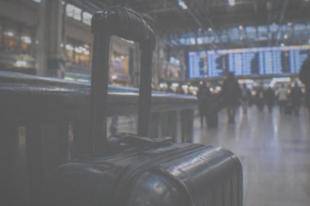 Train station concourse with a long departures board and travellers with rolling bags walking through