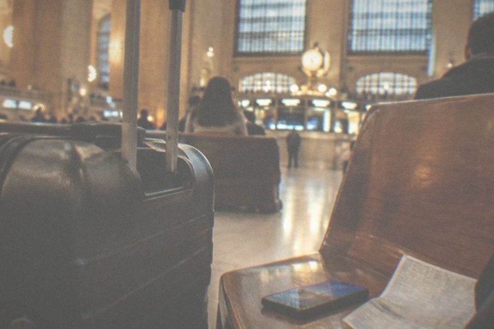 Traveler studying a phone beside a suitcase in a quiet station waiting area