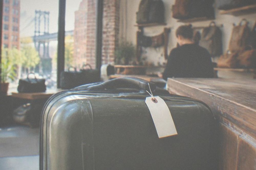 A luggage storage counter worker attaching a numbered tag to a suitcase while a traveller watches