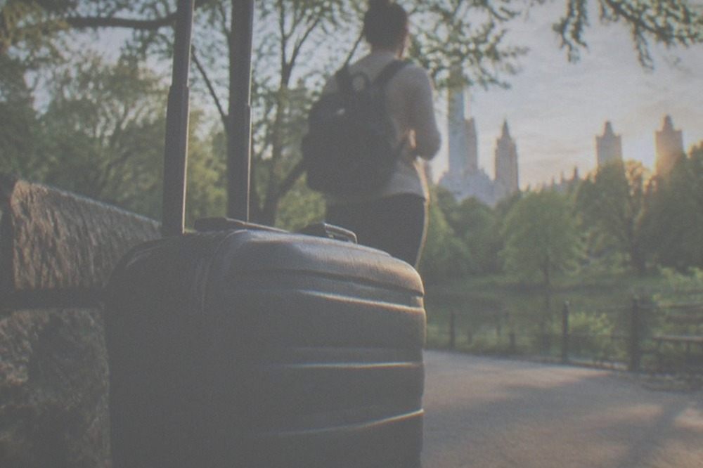 A traveller keeping a small backpack on their shoulder while a large suitcase sits at a counter