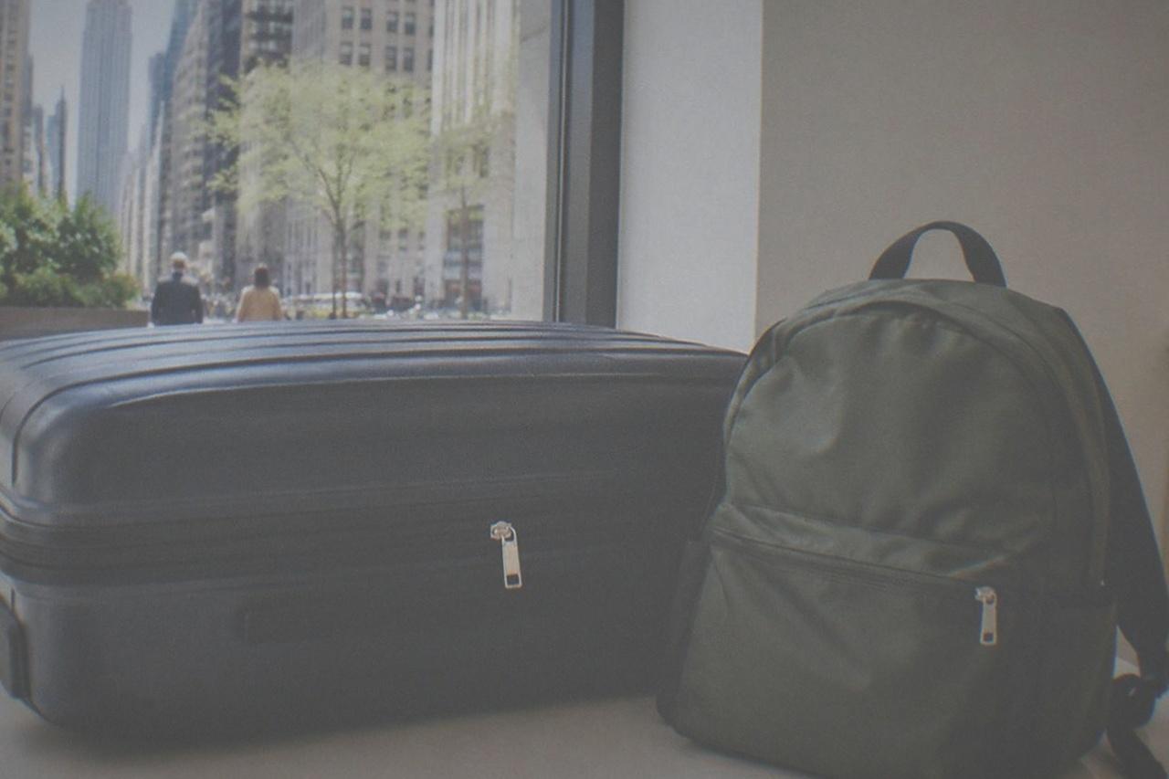 A closed suitcase and a small backpack sitting side by side against a plain wall in a bright shop interior